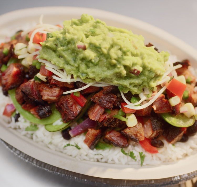 A Smoked Brisket Burrito Bowl with white rice, black beans, fajita veggies, hand-chopped Smoked Brisket, fresh tomato salsa, roasted chili corn salsa, monterey jack shredded cheese, and topped with hand-mashed guac.